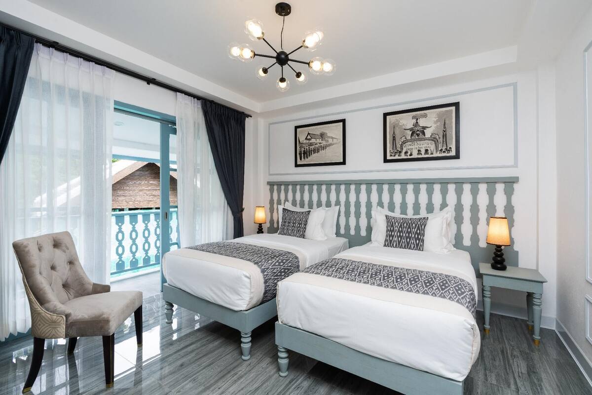 Ein Hotelzimmer mit zwei Betten, einem Sessel, einem Balkon mit Aussicht und zwei gerahmten Bildern an der Wand.