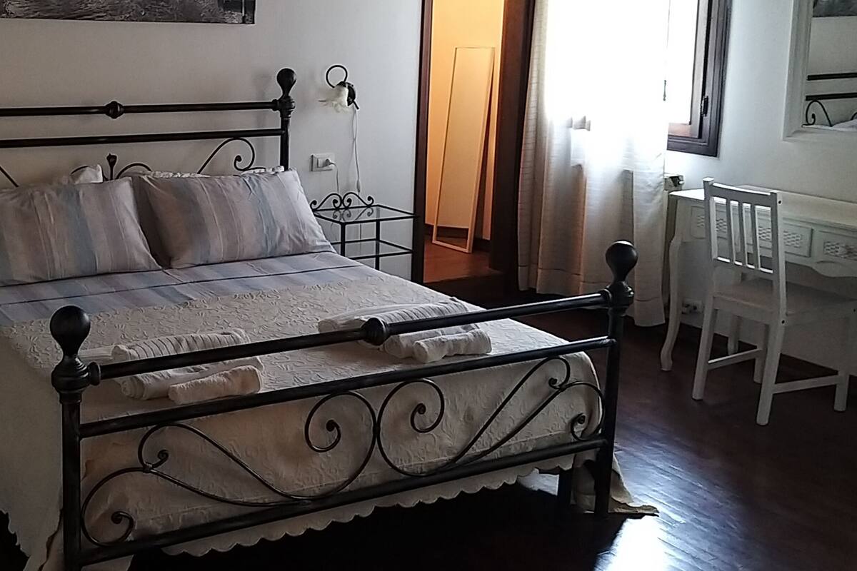 A bed with a metal frame, white bedding, and a small bedside table with a lamp.