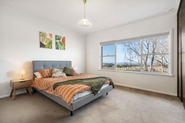 Ein Schlafzimmer mit einem Bett, einem Nachttisch, einer Lampe, einem Fenster mit Blick und Wandkunst.