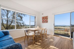 Ein Zimmer mit Esstisch, Stühlen, einer Couch und großen Fenstern mit Blick ins Freie.