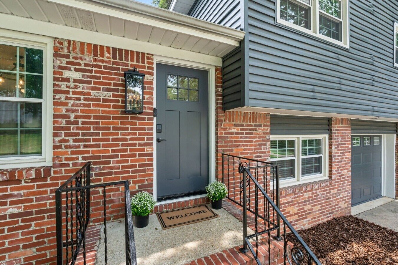 A two-story house with a brick facade, a dark gray front door, and a small front porch with a welcome mat.