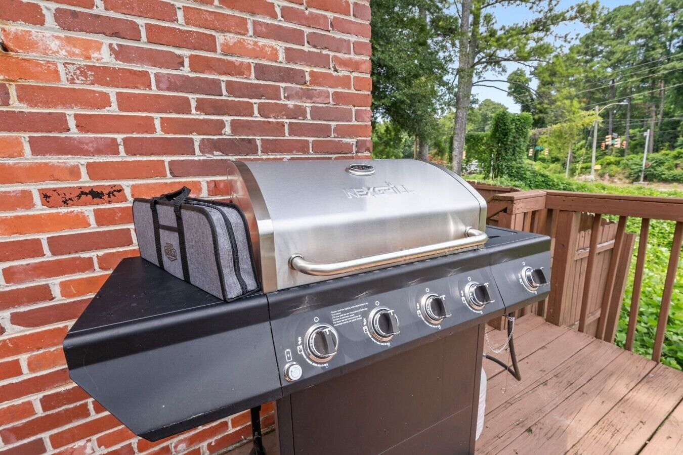 Een barbecue met een extra brander en een geïntegreerde koelbox, voor een bakstenen muur op een houten terras.