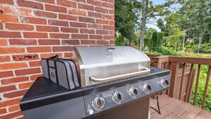 A barbecue grill with a side burner and a built-in cooler, set against a brick wall on a wooden deck. - The Juke Joint: Game Room, Pet-Friendly BHM Home! (Birmingham)
