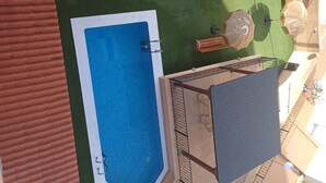 Una piscina en la azotea con agua azul, rodeada por un césped verde y un pequeño espacio de descanso con mesa y sillas.