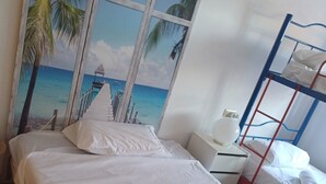 Habitación de hotel con cama, literas y un ventanal con un mural de playa.