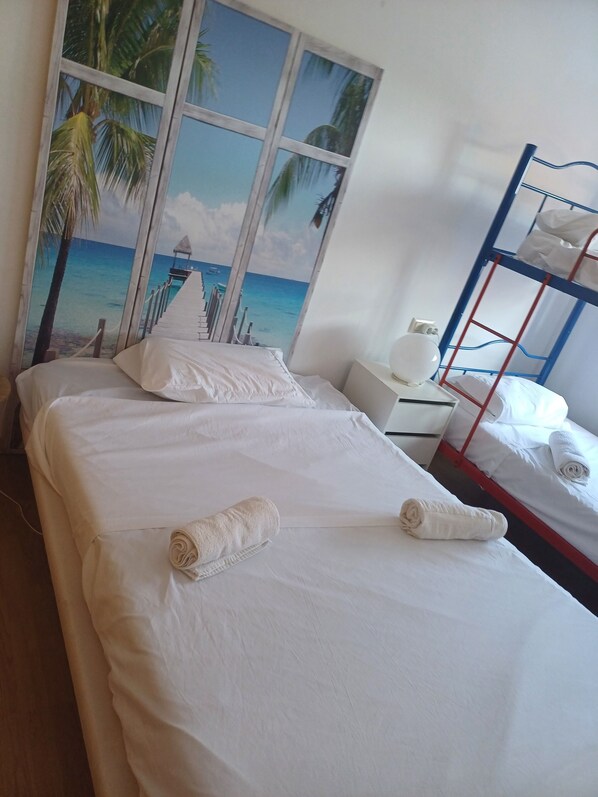 A hotel room with a bed, a bunk bed, and a large window with a beach mural.