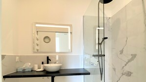 Un baño moderno con ducha de vidrio, lavamanos blanco y espejo sobre la encimera.