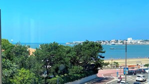 Un paisaje urbano costero con cielo azul despejado, una playa y una carretera que lleva a un estacionamiento.