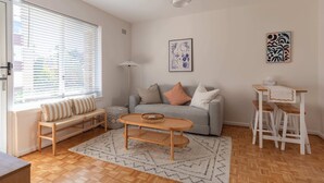 A modern living room with a sofa, a coffee table, and a dining area with stools. - Stylish Sun Drenched North Bondi Beach Oasis (North Bondi)
