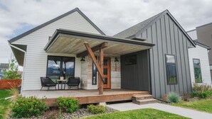 Et moderne hus i to etager med en overdækket veranda, detaljer i sten og en grå facade.