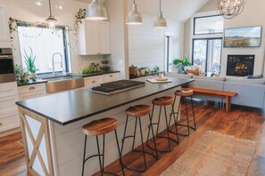 A modern kitchen with a large island, bar stools, and a fireplace. - MSU Access Friendly Fully Loaded Bohemian Design (Bozeman)