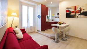 A modern living room with a red sofa, a dining area with white chairs, and a kitchen with red cabinets. - notaMi - Happy Stay - Naviglio Grande (Milan)