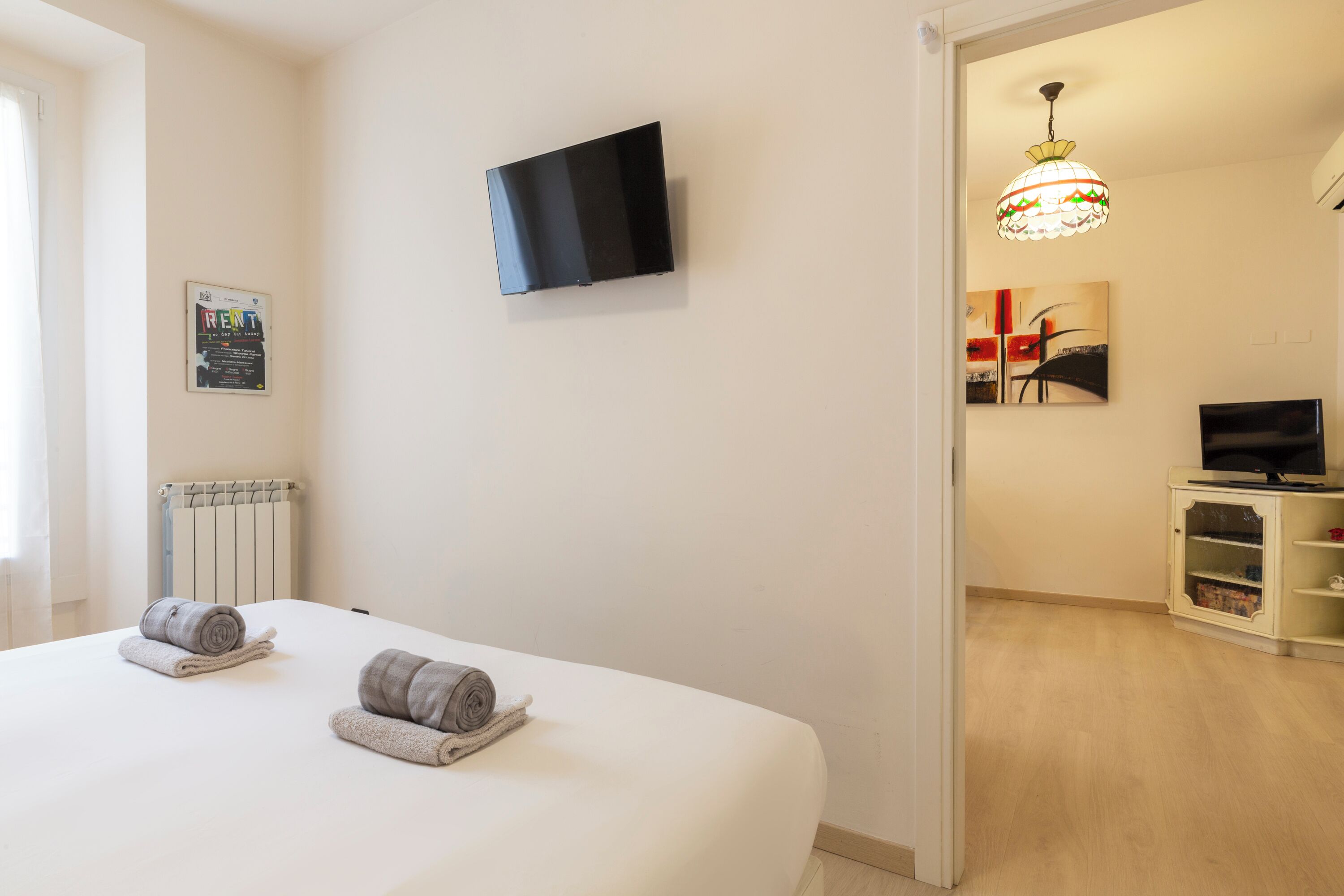 Une chambre d’hôtel avec un lit, un téléviseur fixé au mur, un radiateur et un tableau accroché au mur.