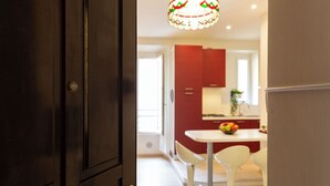 A modern kitchen with white countertops, red cabinets, and a dining area with white chairs. - notaMi - Happy Stay - Naviglio Grande (Milan)