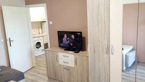 A room with a TV on a wooden cabinet, a washing machine, and a bed. - Sasa Apart (Beograd)