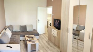 A compact living space with a sofa, a small coffee table, a TV, and a wardrobe. - Sasa Apart (Beograd)