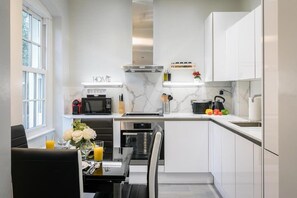 A modern kitchen with white cabinetry, a built-in oven, and a dining area with a table set for two. - Stylish 3-Bedroom Apartment in Greater London (London)
