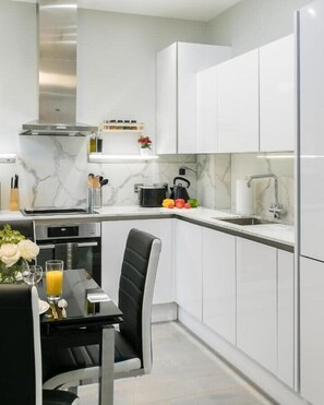 A modern kitchen with white cabinetry, a marble backsplash, and a dining area with a black chair and table.