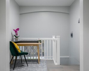Ein Eckzimmer mit einem Holztisch, einem grünen Stuhl mit gelber Sitzkissen, einem gemusterten Teppich und einem weißen Geländer.