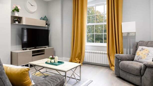 Una sala de estar moderna con una televisión de pantalla plana, un sofá, una mesa de centro y una ventana con cortinas amarillas.