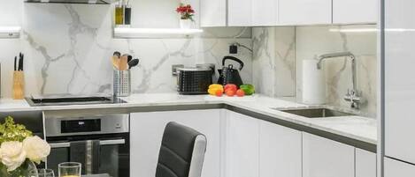 Eine moderne Küche mit weißen Schränken, einer Marmor-Spritzschutzleiste und einem Essbereich mit schwarzem Stuhl und Tisch.