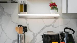 Una cocina con salpicadero de mármol, un estante para especias, un hervidor y una tabla de cortar con verduras.