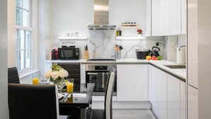 Una cocina moderna con muebles blancos, horno integrado y un comedor con mesa para dos.