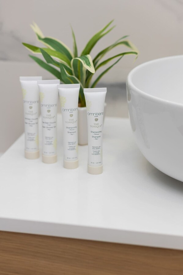Quatre bouteilles de shampooing pour cheveux de la marque « omnisens » sont posées sur une surface blanche, avec un bol blanc et une plante en pot en arrière-plan.