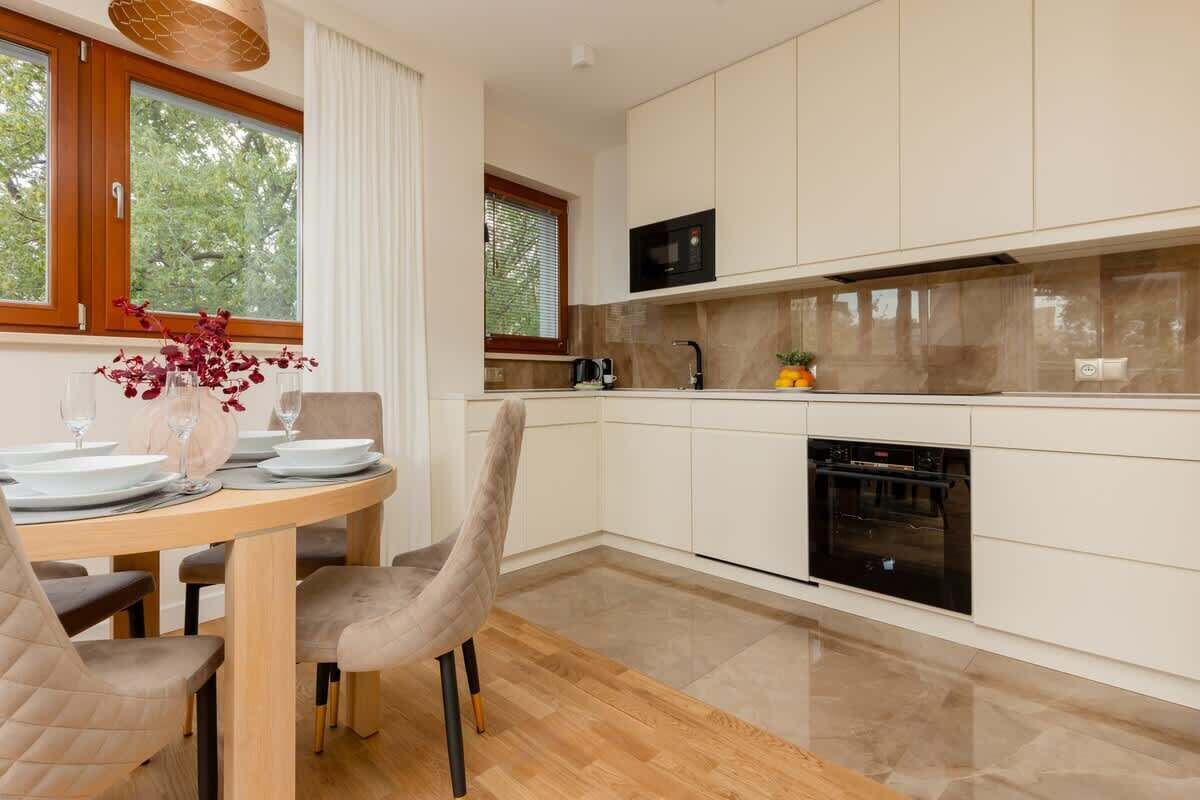 A modern kitchen with white cabinets, a microwave, and an oven. There is a dining table with chairs and a vase with flowers.