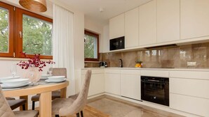 Une cuisine moderne avec des meubles blancs, un four à micro-ondes et un four traditionnel. On y trouve une table à manger avec des chaises et un vase rempli de fleurs.