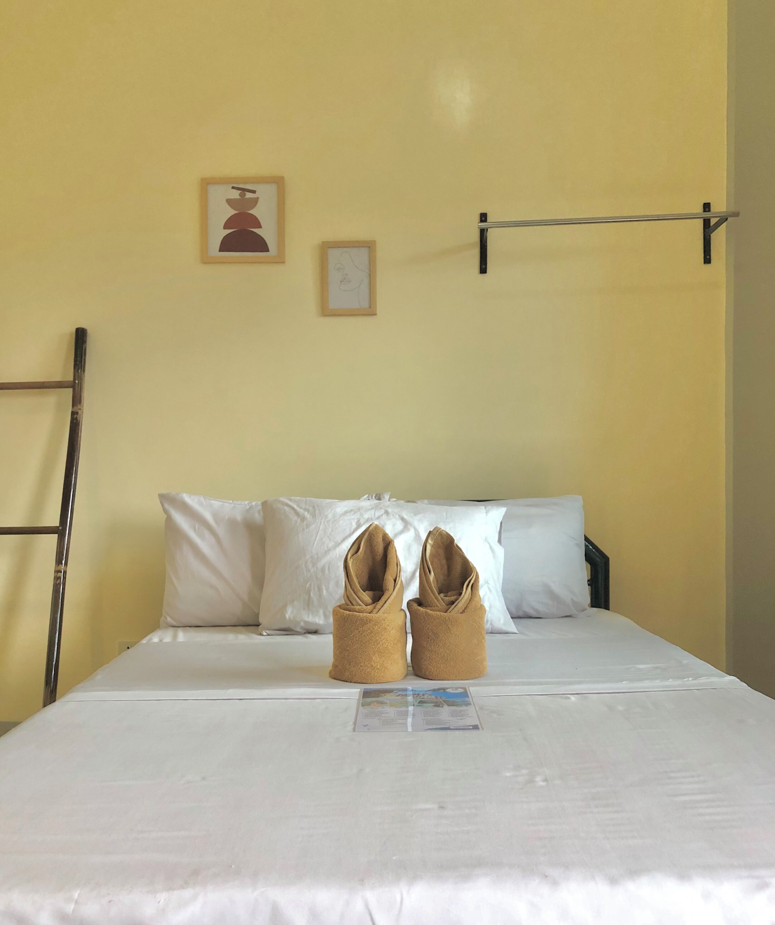 A neatly made bed with a white sheet, two rolled towels, and a small informational card on the bed.