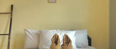 A neatly made bed with a white sheet, two rolled towels, and a small informational card on the bed.