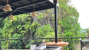 An outdoor coffee station with a stainless steel espresso machine, a glass carafe, and a coffee grinder. There are hanging wicker lamps and a view of lush greenery and a rocky cliff in the background. - Hannas Inn El Nido Palawan  (El Nido)