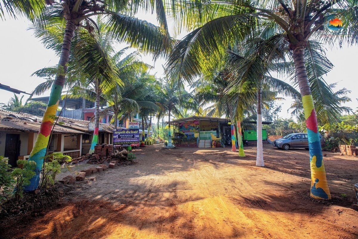A reception area with a dirt path leading to a building, surrounded by palm trees and a signboard.