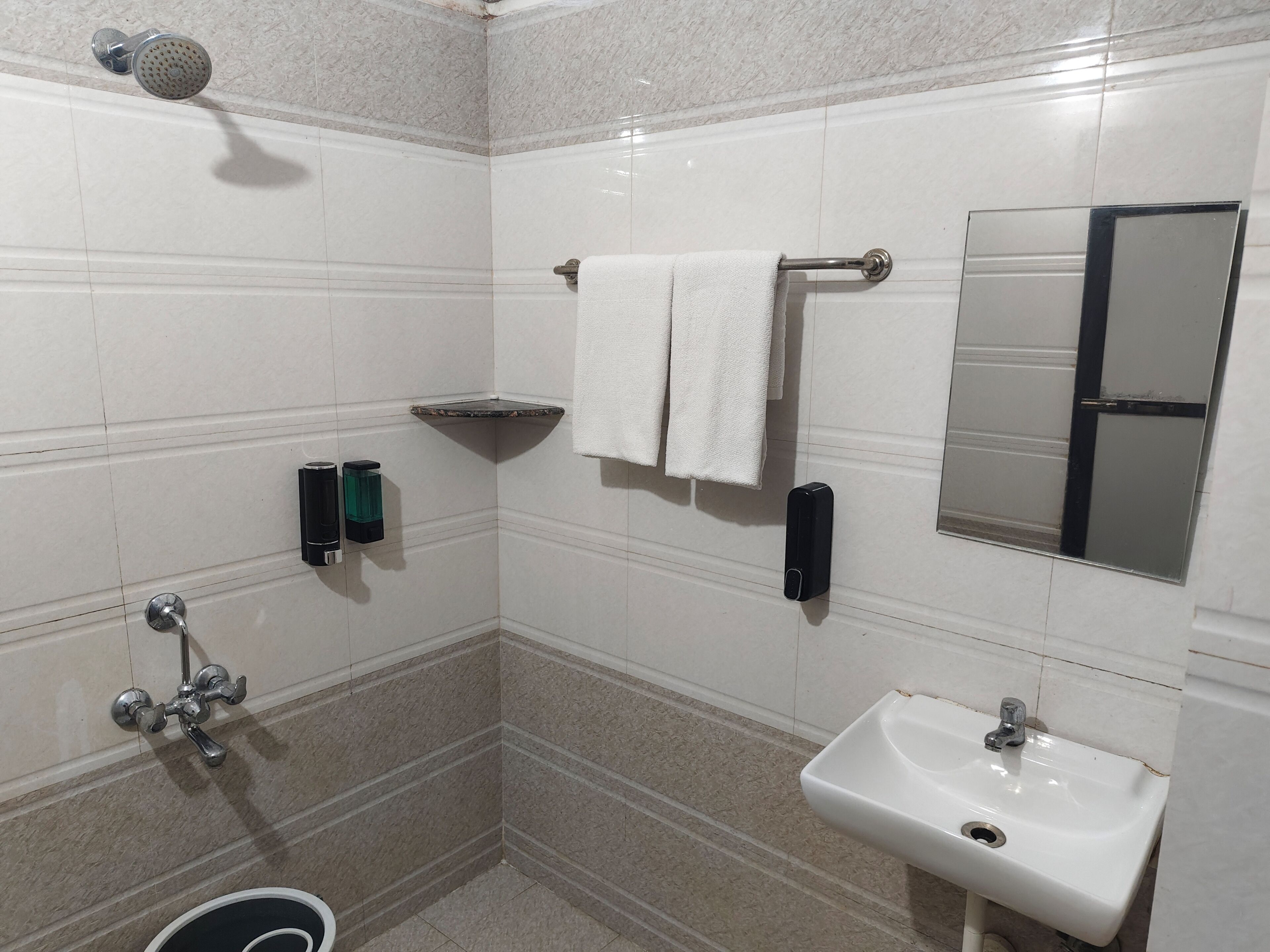 Un baño con ducha, lavamanos, toallero y espejo.