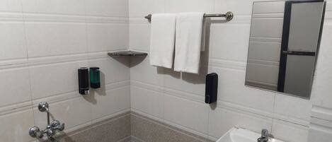 Un baño con ducha, lavamanos, toallero y espejo.