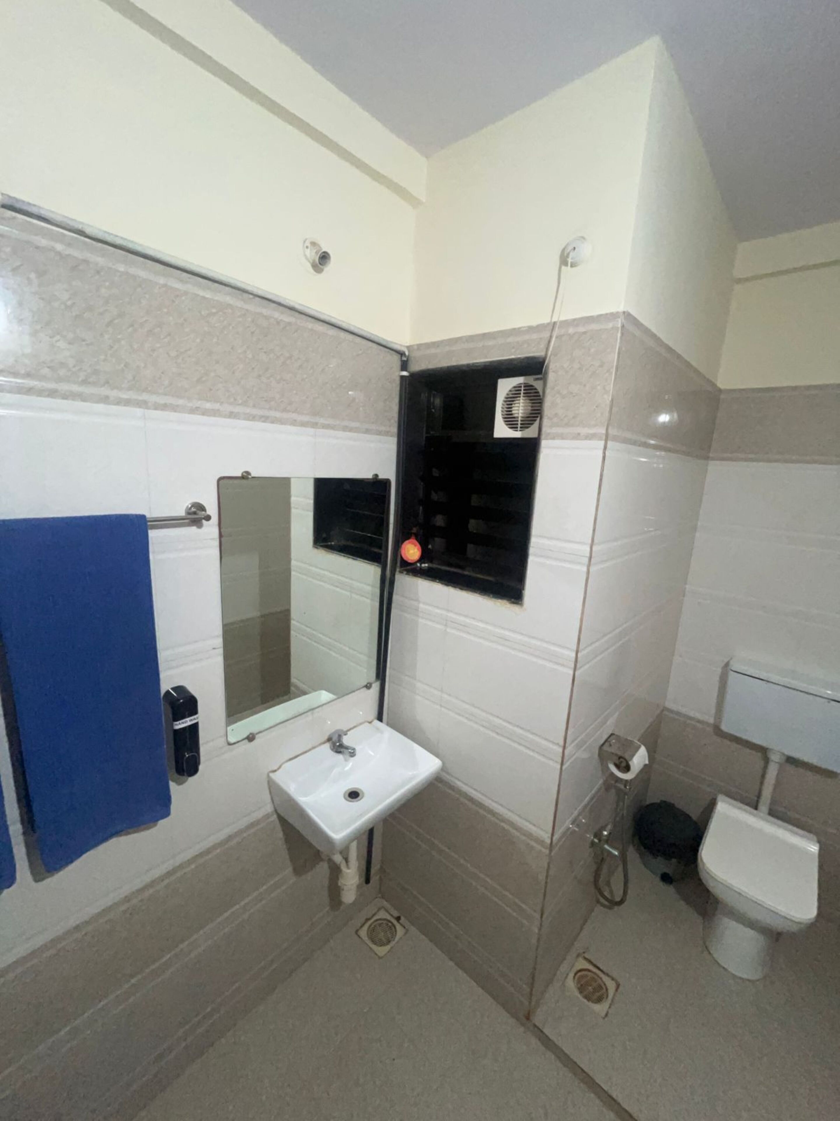 Casa de banho com lavatório branco, espelho, toalha azul, sanita e zona de duche.