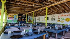 Un restaurante con varias mesas y sillas, techo de madera y paredes decoradas con imágenes y texto relacionados con la comida.