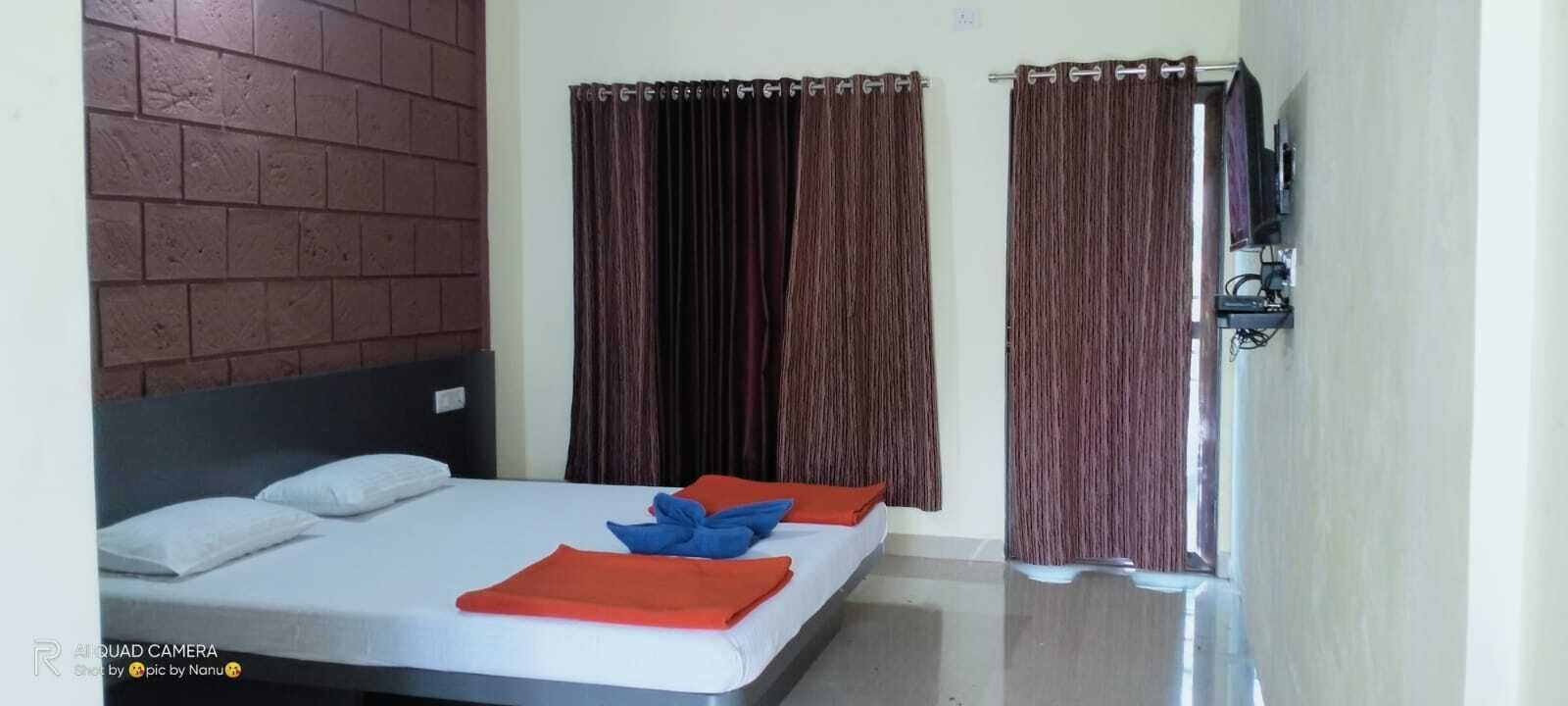 A hotel room with a bed, two pillows, a blanket, and curtains.