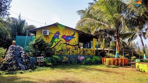 Un edificio colorido con un mural de aves y mariposas, rodeado de abundante vegetación y palmeras.