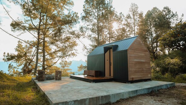 Une petite cabane avec un toit en pente, une façade en bois et une plateforme en béton sur laquelle se trouve un banc.
