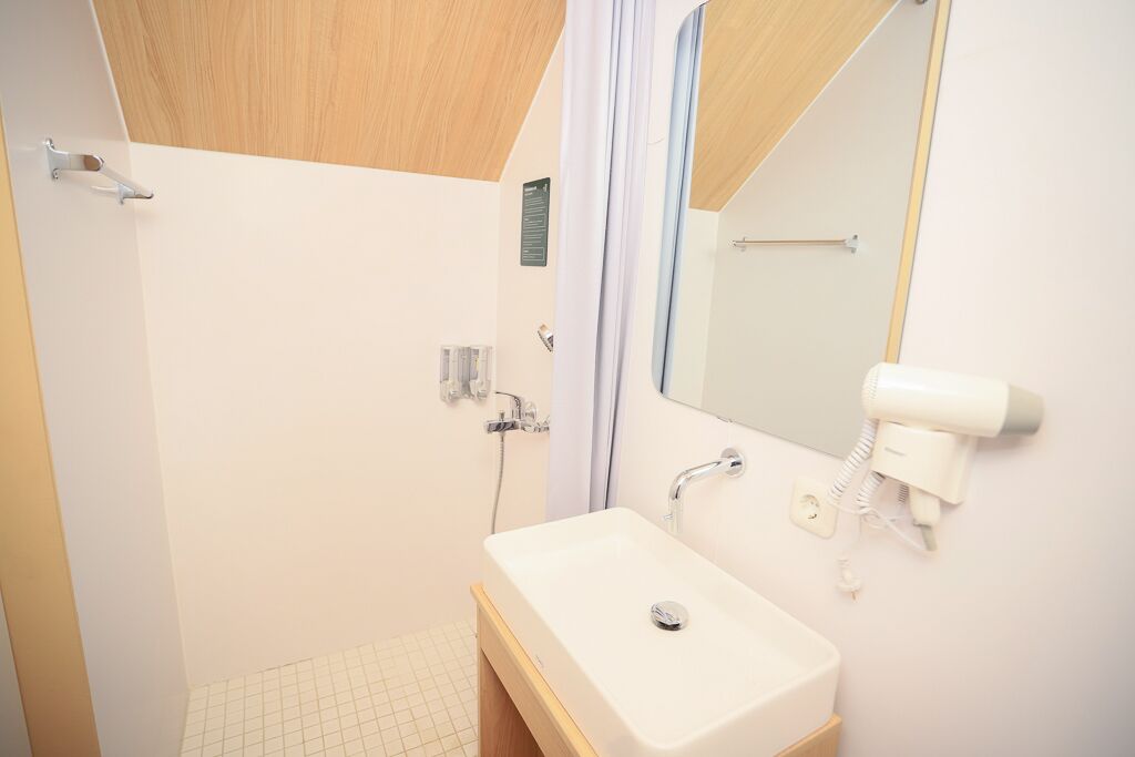Un baño con ducha, lavamanos, secador de pelo y espejo.