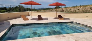 Una piscina con dos sombrillas rojas, tres tumbonas de madera y vistas a un paisaje montañoso.
