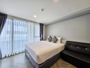 A modern hotel room with a large bed, a black leather sofa, and sheer curtains on the windows. - 14 Sathorn hotel (Bangkok)
