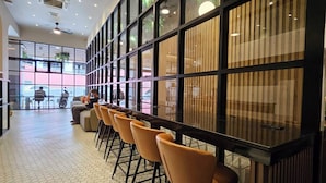 A modern indoor seating area with a long counter and orange chairs, large windows, and a tiled floor. - 14 Sathorn hotel (Bangkok)