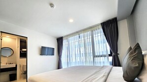A modern hotel room with a large bed, a TV mounted on the wall, a bathroom with a mirror and sink, and a window with curtains. - 14 Sathorn hotel (Bangkok)