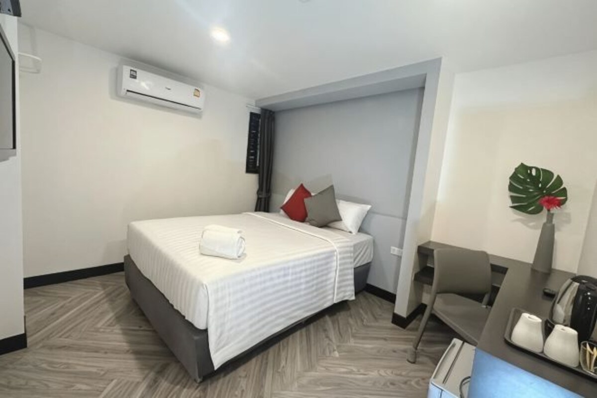 Une chambre d’hôtel équipée d’un lit, d’un bureau, d’une chaise, d’un climatiseur et d’une plante décorative.