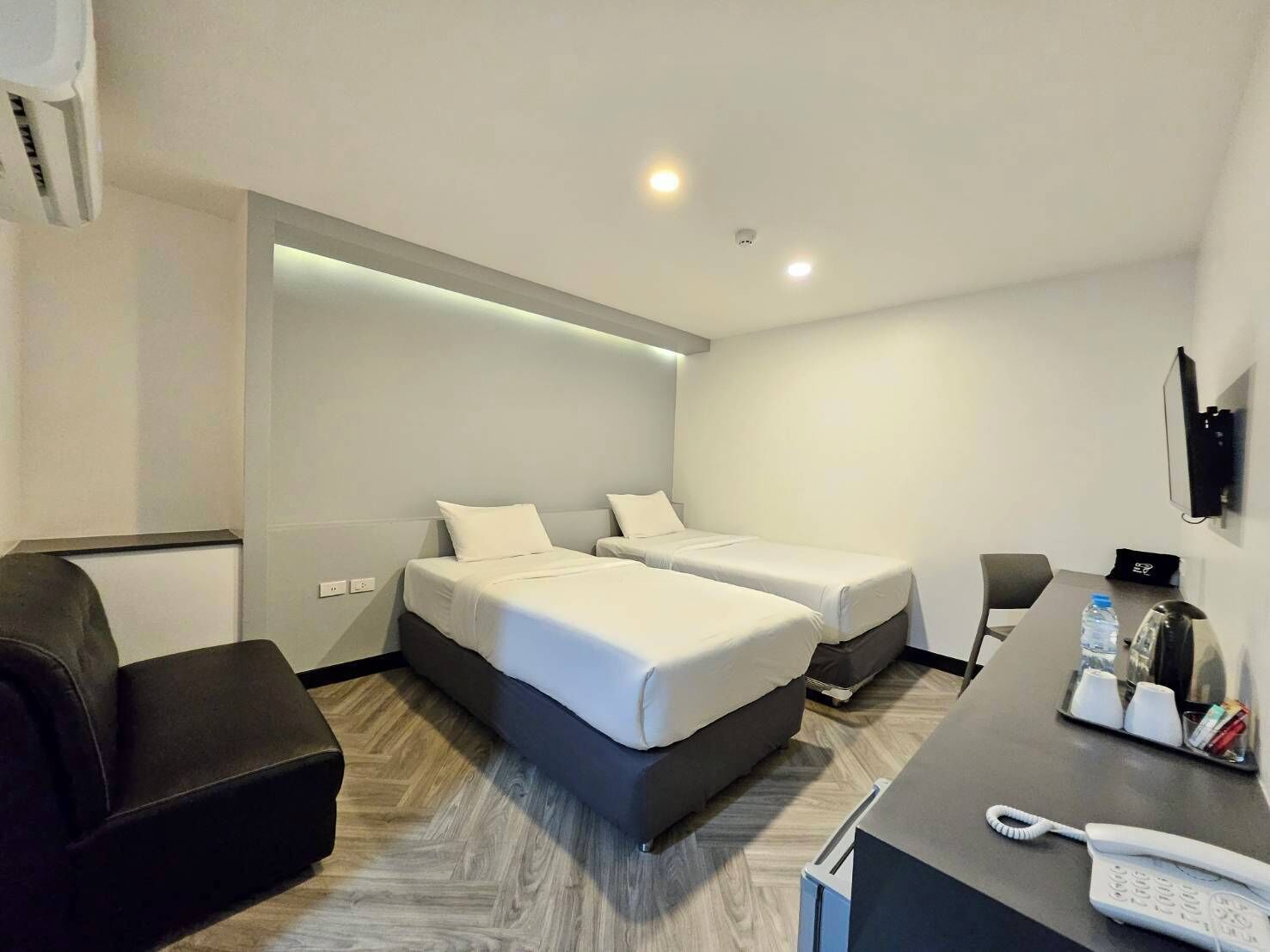 A modern hotel room with two beds, a desk with a phone, a chair, and a TV mounted on the wall.