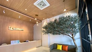 A reception area with a wooden reception desk, a sofa with cushions, a large artificial tree, and a ceiling fan. - 14 Sathorn hotel (Bangkok)
