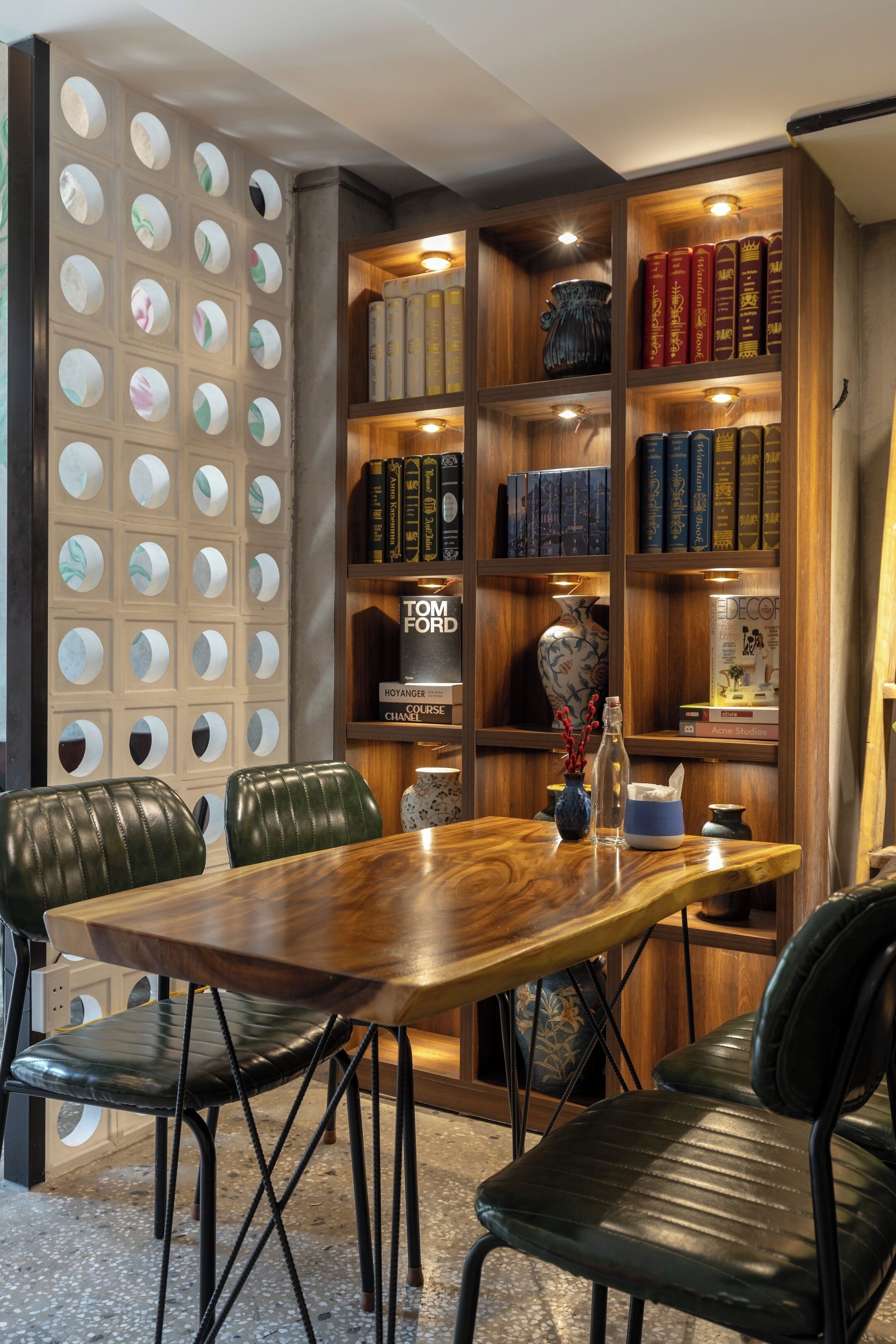 A wooden dining table with leather chairs, surrounded by bookshelves with various books and decorative items.